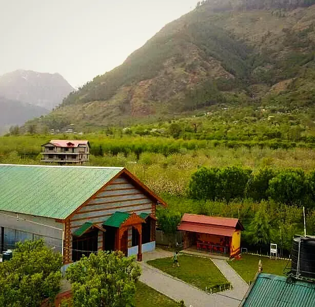 A green-roofed cottage among apple orchards below the mountains